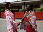 Kaksi perinteisiin pukuihin pukeutunutta Maasai-naista kättelevät.